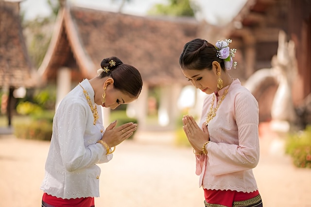 Deux femmes en costume traditionnel thaïlandais effectuent le wai, geste de salutation et de respect