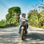 Deux personnes à scooter sur une route de campagne en Thaïlande sous le soleil