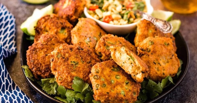 Assiette de galettes de poisson frites Tod Man Pla, servies sur un lit de coriandre avec une sauce aux cacahuètes et concombre en accompagnement.