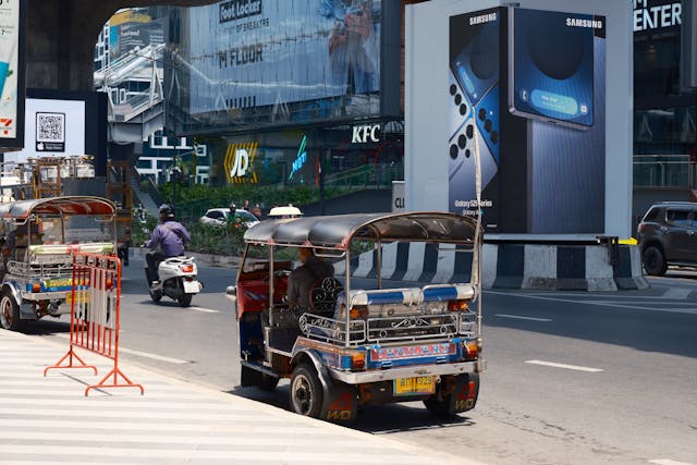 Tuk-tuk stationné en bord de route devant un centre commercial moderne à Bangkok