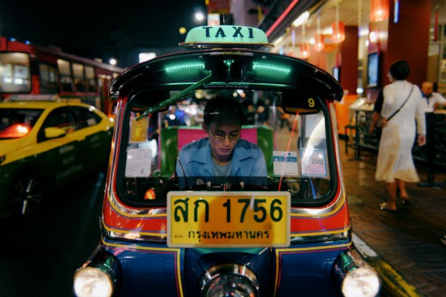 Tuk-tuk coloré dans les rues animées de Bangkok la nuit, chauffeur au volant