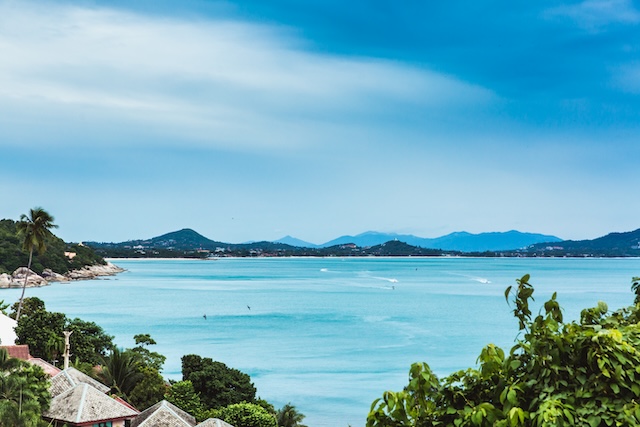 Vue panoramique sur la baie de Koh Samui avec mer turquoise, toits traditionnels et montagnes en arrière-plan