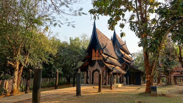 Structure en bois sombre de style Lanna de la Baan Dam (Maison Noire) à Chiang Rai, l'œuvre de l'artiste Thawan Duchanee, située dans un parc arboré.