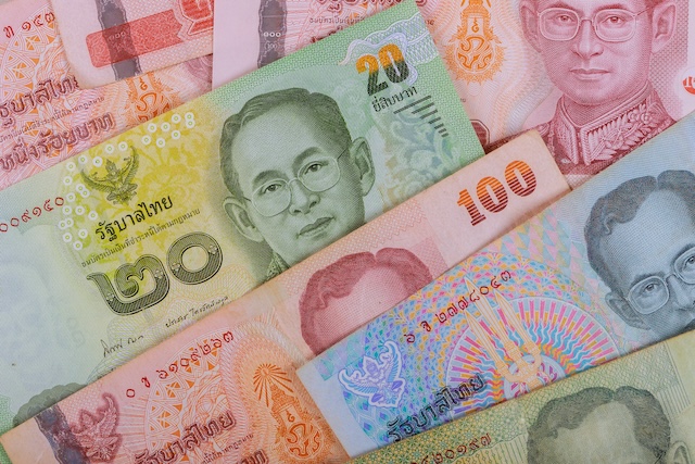 Gros plan sur un assortiment de billets de Baht thaïlandais de différentes couleurs et valeurs (20, 100 Baht), montrant le portrait du roi de Thaïlande.