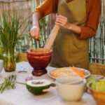 Deux personnes préparant une salade de papaye verte (Som Tum) dans un mortier en bois lors d'un cours de cuisine en plein air en Thaïlande.