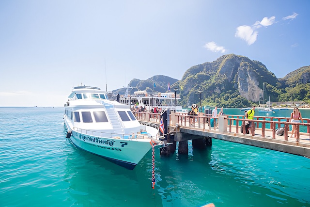 Ferry de touristes accosté au quai de Tonsai Pier à Koh Phi Phi Don, avec des voyageurs marchant sur la jetée sous un ciel bleu et les montagnes de l'île en arrière-plan.