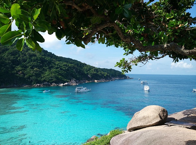 Vue panoramique depuis le point de vue de "Sail Rock" sur une baie aux eaux turquoise des îles Similan, avec des bateaux de plongée au mouillage.