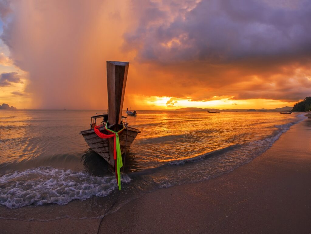 Image de couverture pour l'itinéraire de 3 semaines en Thaïlande : un bateau long-tail sur une plage de sable au coucher du soleil.