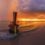 Image de couverture pour l'itinéraire de 3 semaines en Thaïlande : un bateau long-tail sur une plage de sable au coucher du soleil.