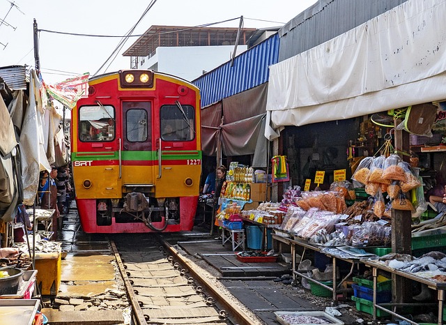 Train rouge et jaune traversant le marché ferroviaire de Maeklong en Thaïlande, avec des étals de produits locaux installés sur les voies.