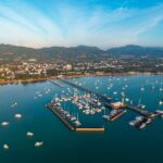 Vue aérienne de la marina de Chalong à Phuket, remplie de yachts et de bateaux d'excursion, avec la jetée s'avançant dans la mer et le Grand Bouddha visible sur les collines.