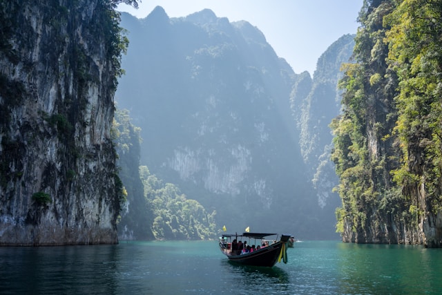 Bateau long-tail naviguant sur les eaux émeraudes du lac Cheow Lan dans le Parc National de Khao Sok, entouré de majestueuses falaises karstiques et de jungle.