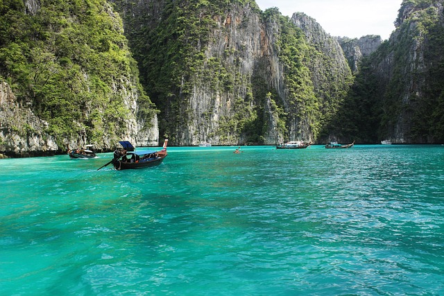 Bateau long-tail naviguant sur l'eau turquoise de Pileh Lagoon à Koh Phi Phi, entouré par d'imposantes falaises calcaires couvertes de végétation.