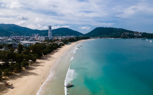 Vue aérienne de la plage de Patong à Phuket, montrant la longue baie de sable, l'eau turquoise et la ville en arrière-plan.