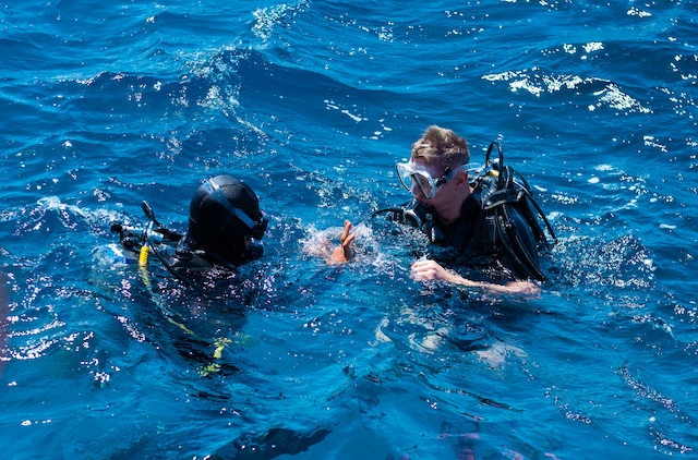 Deux plongeurs avec bouteilles et masques communiquant en surface, prêts à plonger dans les eaux bleues de Thaïlande.