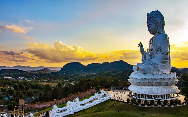 Vue spectaculaire de la statue géante de Guan Yin au Wat Huay Pla Kang à Chiang Rai, avec les montagnes en arrière-plan au coucher du soleil.