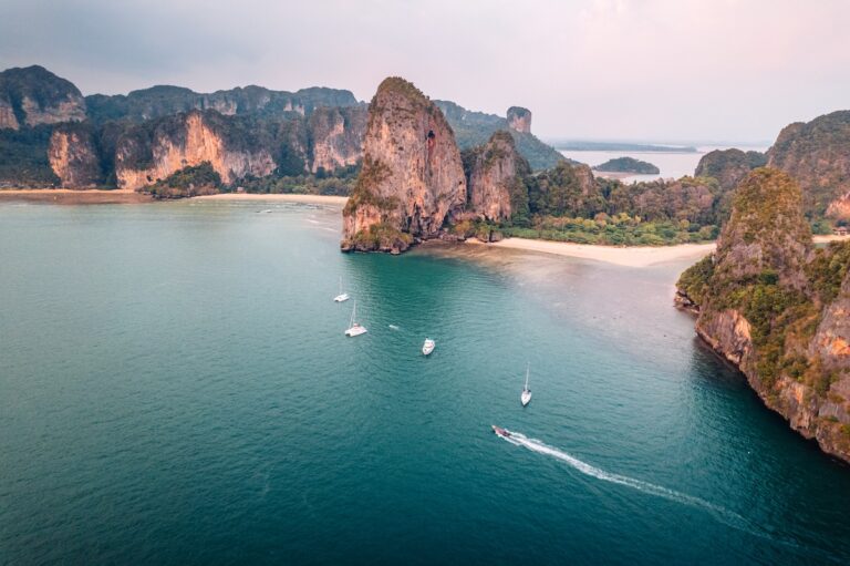 Vue aérienne des falaises karstiques de la plage de Railay à Krabi, en Thaïlande, avec des bateaux sur une mer turquoise et une plage de sable blanc.