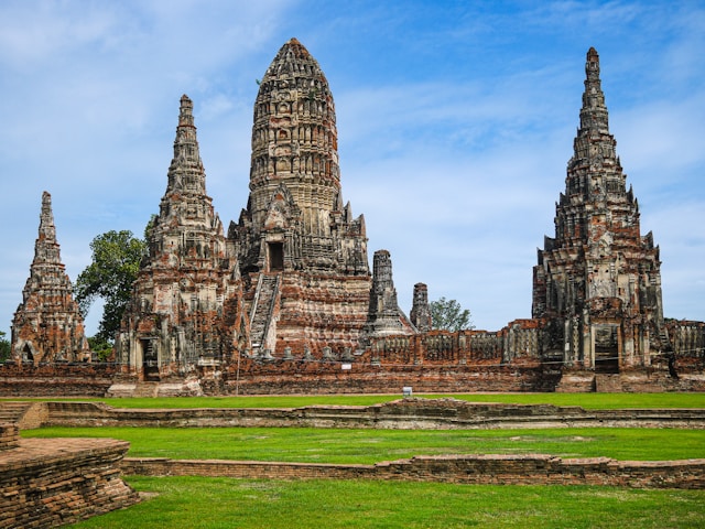 Vue d'ensemble du temple Wat Chaiwatthanaram à Ayutthaya, montrant son grand prang central de style khmer et ses tours environnantes sur une pelouse verte.