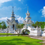 Pavillons blancs et pont du Wat Rong Khun à Chiang Rai, entourés de verdure sous un ciel bleu