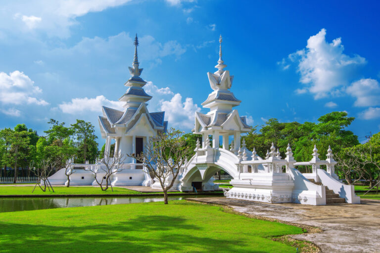 Pavillons blancs et pont du Wat Rong Khun à Chiang Rai, entourés de verdure sous un ciel bleu