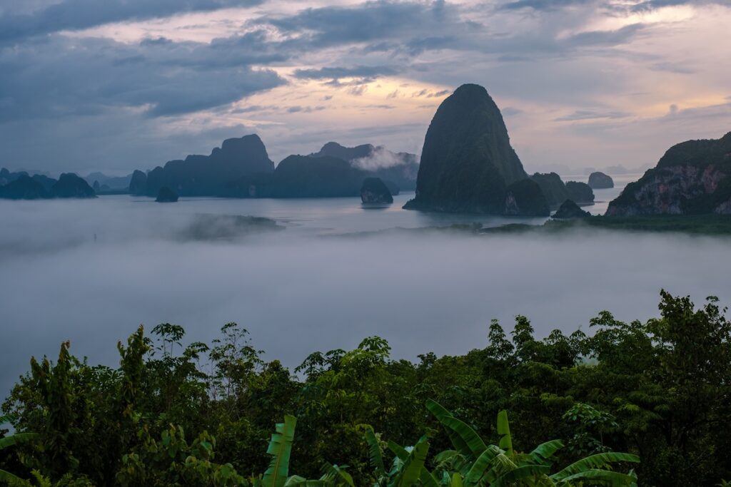 Vue panoramique des îles karstiques de la baie de Phang Nga en Thaïlande, émergeant d'une épaisse couche de brume matinale au lever du soleil.