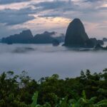 Vue panoramique des îles karstiques de la baie de Phang Nga en Thaïlande, émergeant d'une épaisse couche de brume matinale au lever du soleil.