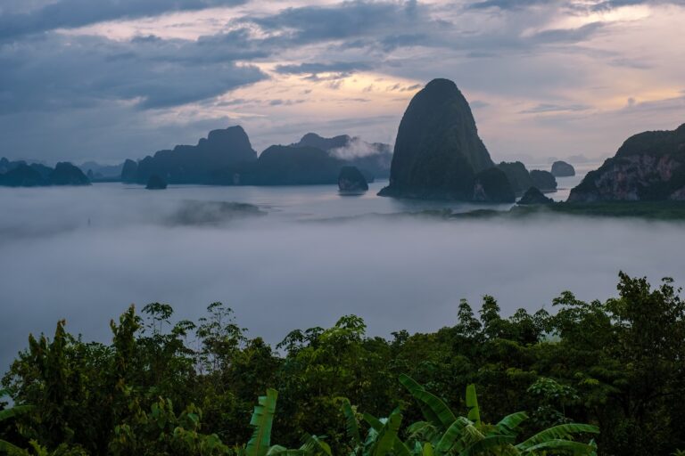 Vue panoramique des îles karstiques de la baie de Phang Nga en Thaïlande, émergeant d'une épaisse couche de brume matinale au lever du soleil.