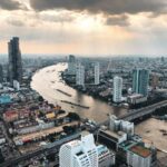 Vue aérienne de la ville de Bangkok au coucher du soleil, montrant le fleuve Chao Phraya, les gratte-ciels et les ponts, illustrant le coût de la vie et l'installation dans la capitale thaïlandaise.