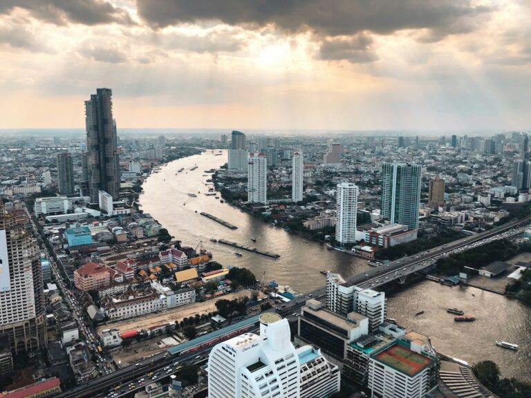 Vue aérienne de la ville de Bangkok au coucher du soleil, montrant le fleuve Chao Phraya, les gratte-ciels et les ponts, illustrant le coût de la vie et l'installation dans la capitale thaïlandaise.