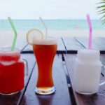 Trois verres de boissons thaïlandaises colorées, un jus de fruit, un thé glacé et un smoothie coco, sur une table face à la mer.