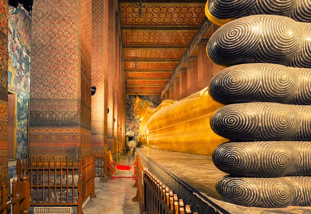 Vue intérieure du temple Wat Pho à Bangkok, montrant l'imposante statue dorée du Bouddha couché et les détails des piliers décorés.
