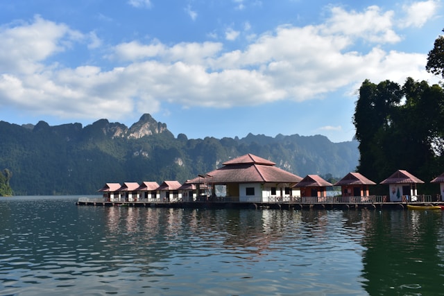 Vue des bungalows flottants sur les eaux calmes du lac de Khao Sok, avec les montagnes karstiques en arrière-plan sous un ciel bleu nuageux.