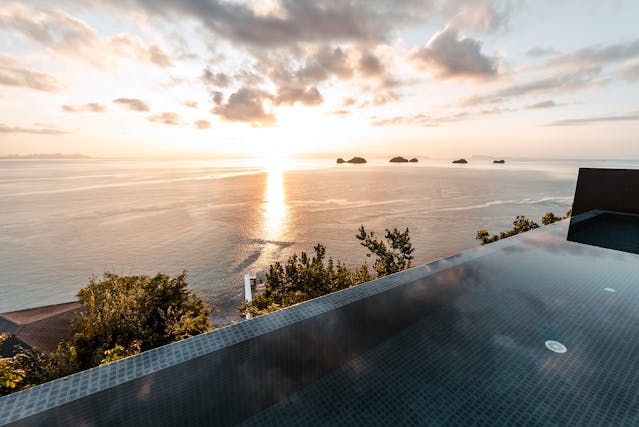 Vue depuis la piscine à débordement d'une villa de luxe sur la mer et les îles thaïlandaises au crépuscule, illustrant le style de vie pour les expatriés à Phuket ou Koh Samui.