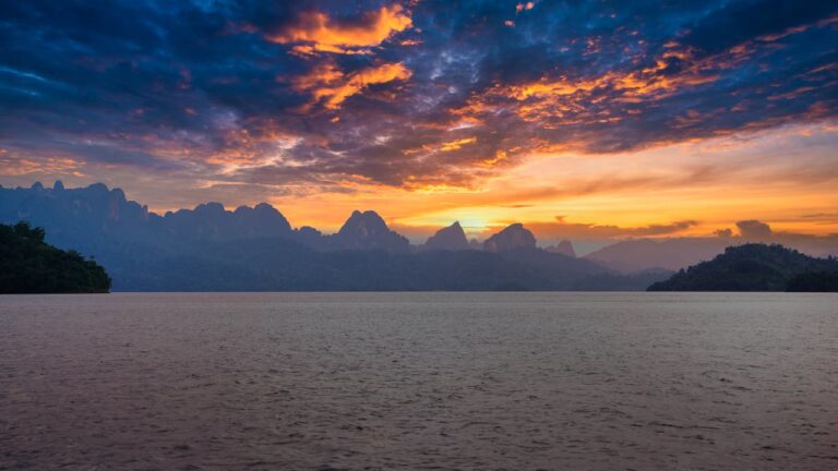 Coucher de soleil spectaculaire avec des nuages orange et bleus au-dessus des montagnes karstiques du parc national de Khao Sok, une expérience insolite en Thaïlande.