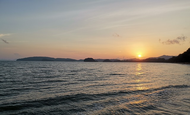 Coucher de soleil sur la mer en Thaïlande, avec le soleil se reflétant sur l'eau et des îles en silhouette à l'horizon.