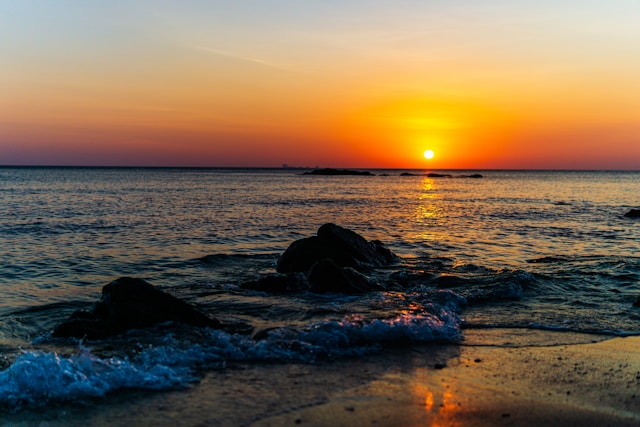Coucher de soleil orange sur la mer d'Andaman avec des rochers au premier plan sur une plage de Koh Lanta.