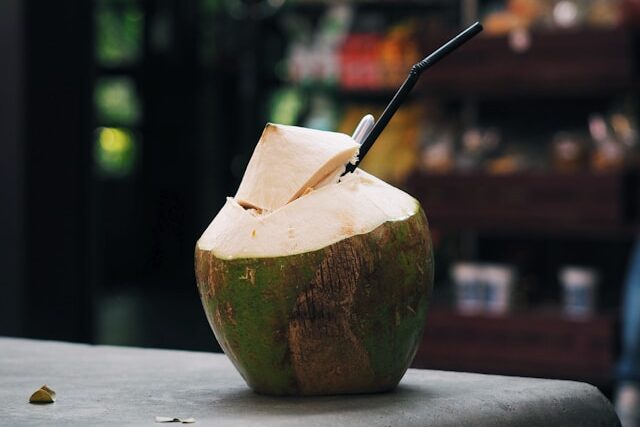 Une noix de coco verte fraîche, ouverte sur le dessus avec une paille, posée sur un muret en pierre en Thaïlande.