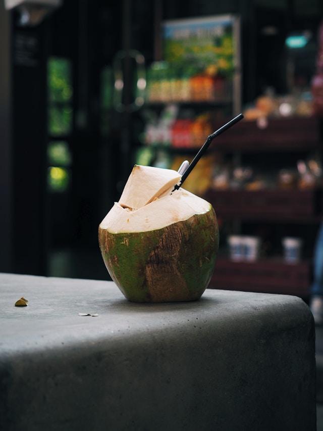 Une noix de coco verte fraîche, ouverte sur le dessus avec une paille, posée sur un muret en pierre en Thaïlande.