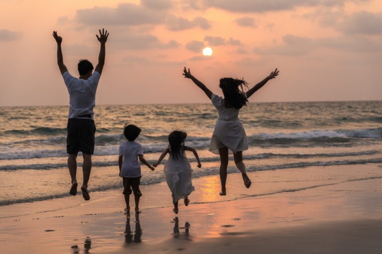 Silhouette d'une famille avec deux enfants sautant et courant joyeusement sur une plage au bord de la mer, avec le soleil se couchant sur l'horizon.