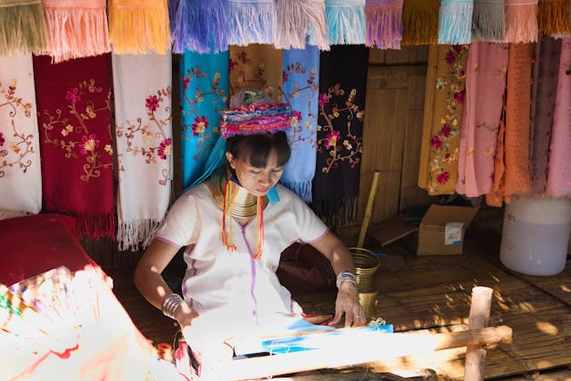 Une femme Karen au long cou, avec ses anneaux traditionnels en laiton, tisse de l'artisanat coloré dans un village près de Chiang Rai.
