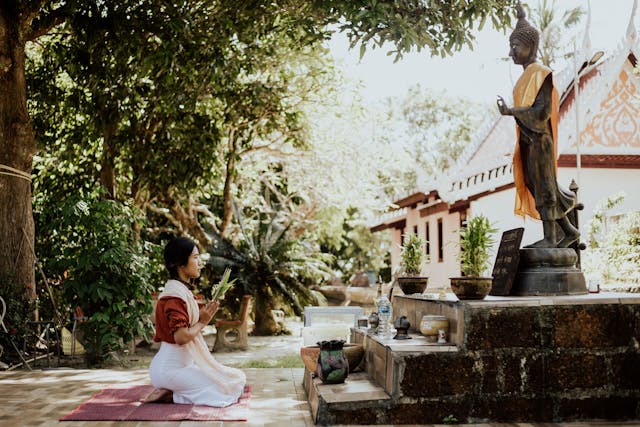 Une femme thaïlandaise à genoux sur un tapis de prière fait une offrande devant une statue de Bouddha dans la cour d'un temple en Thaïlande.
