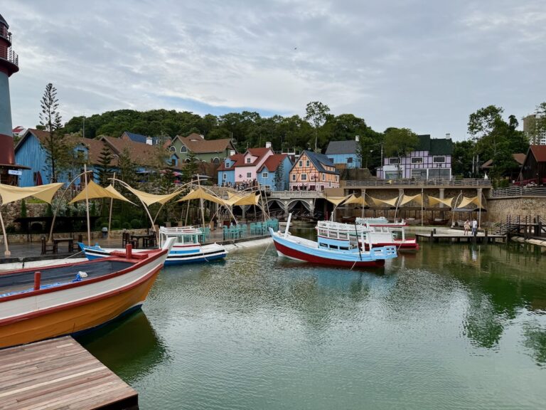 Vue d'ensemble du Fisherman Village à Pattaya, montrant des bateaux de pêche colorés sur un plan d'eau devant des bâtiments de style scandinave et des terrasses de restaurants.