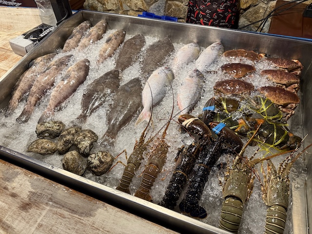 Étal de fruits de mer frais sur un lit de glace au Fisherman Village Pattaya, avec poissons, huîtres, crabes et langoustes prêts à être cuisinés.