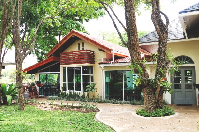 Bâtiment d'une guesthouse ou d'un restaurant avec une grande baie vitrée et une terrasse, entouré d'un jardin et d'arbres près du parc national de Khao Yai.