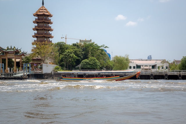 Bateau à longue queue traditionnel naviguant sur le fleuve Chao Phraya à Bangkok, avec une pagode en arrière-plan