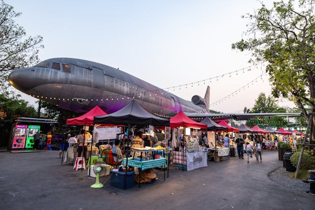 Vue du marché de nuit Chang Chui à Bangkok, avec ses stands colorés installés sous l'aile d'un grand avion abandonné et illuminé.