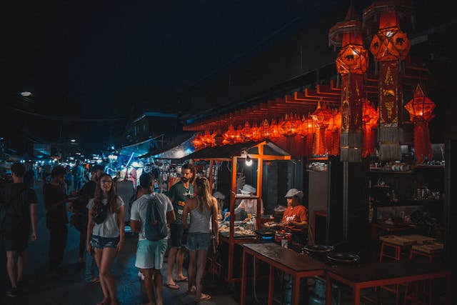 Foule de touristes et locaux déambulant au marché de nuit de Pai, avec des stands de street food illuminés par des lampions traditionnels thaïlandais.