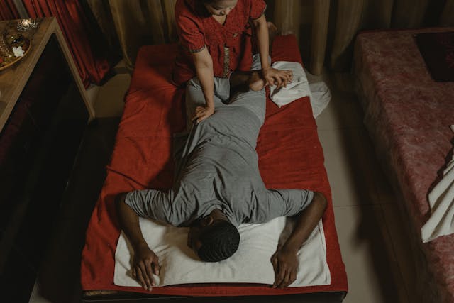 Vue de dessus d'un homme recevant un massage thaïlandais par une praticienne dans un salon de massage à l'ambiance tamisée.