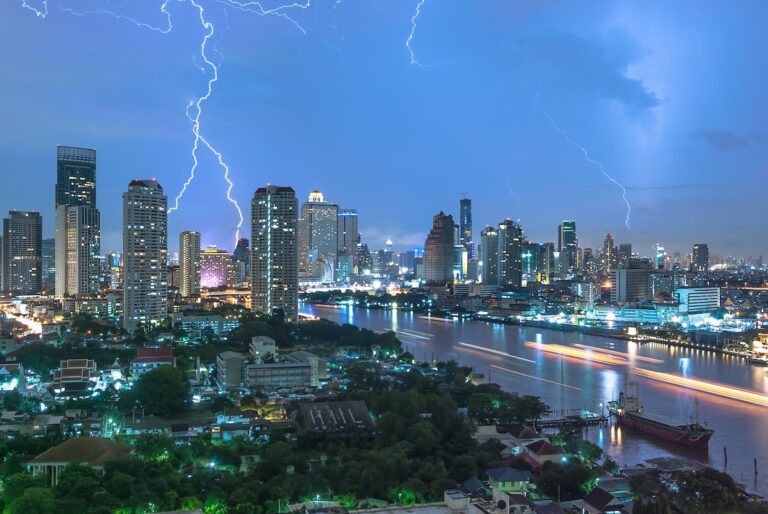 Vue panoramique de la skyline de Bangkok la nuit pendant un violent orage, avec de multiples éclairs illuminant le ciel au-dessus du fleuve Chao Phraya.