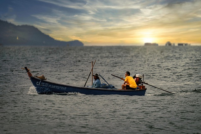 Deux hommes sur un bateau de pêche local en Thaïlande naviguant sur la mer au coucher du soleil, symbolisant l'aventure d'un voyage authentique.